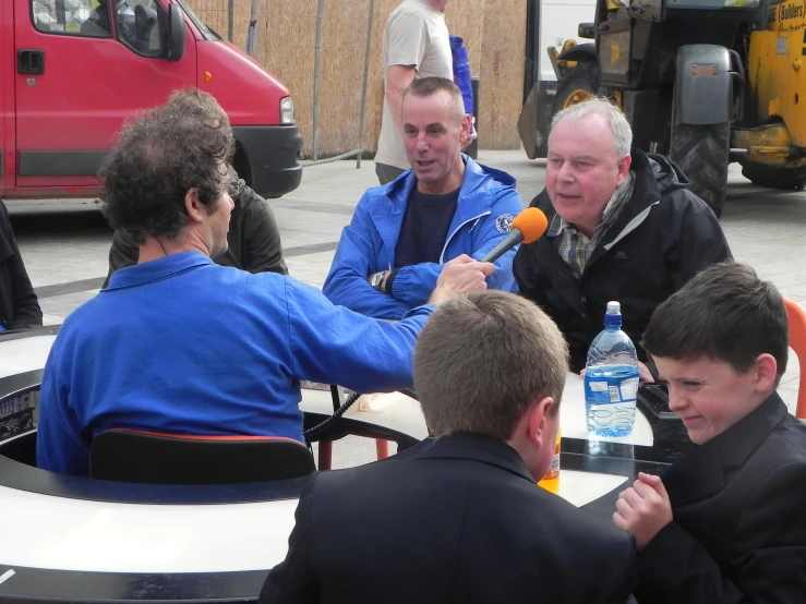 three men in jackets are gathered around a table having drinks