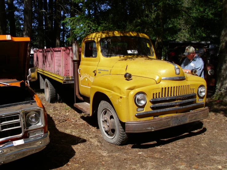 two people sitting beside a yellow truck and a forest