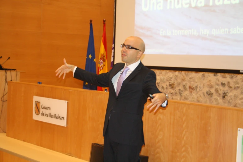 a man in a business suit standing at a podium giving a presentation