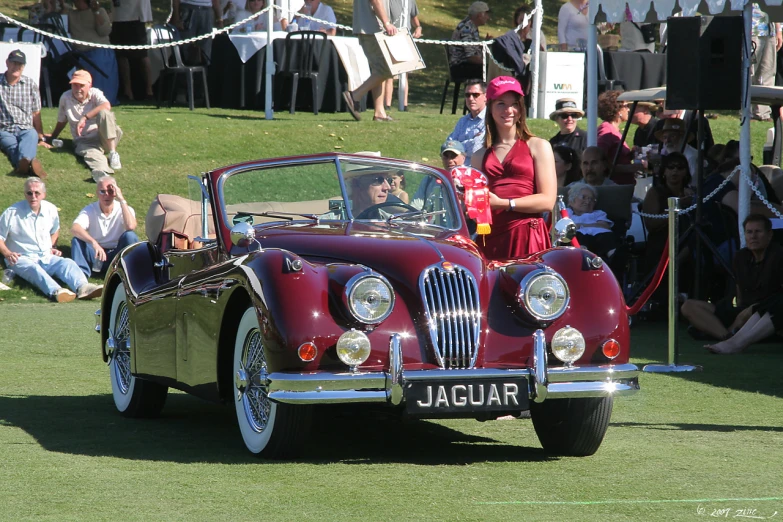 two women standing behind a car with the word jaguar on it