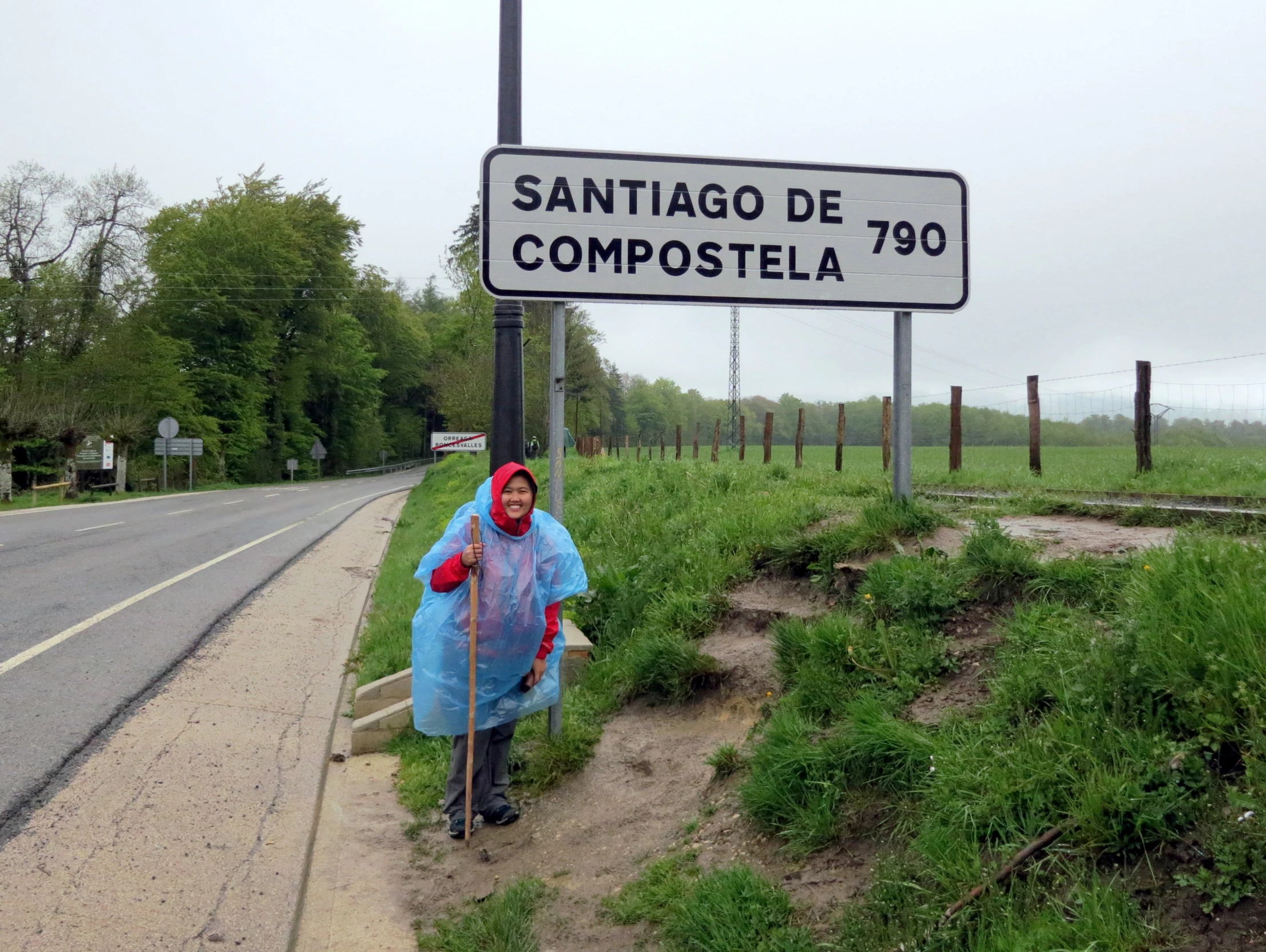 a woman is in a blue raincoat near a road sign