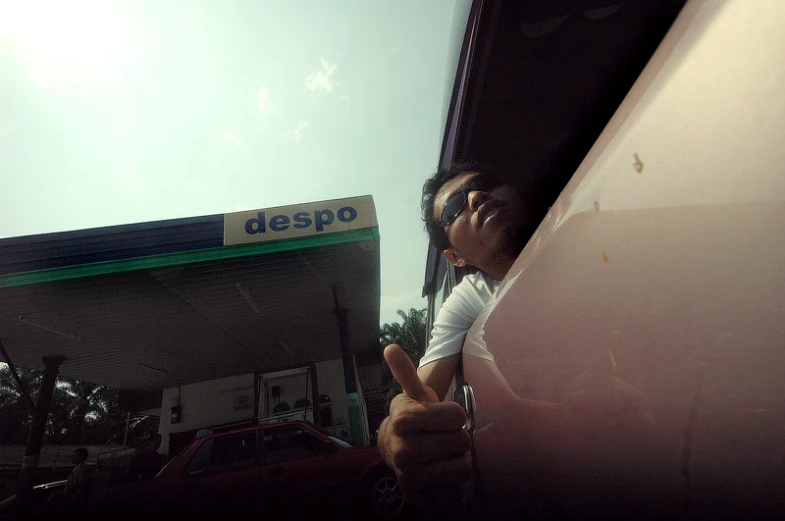 woman holding up thumbs in front of the gas station