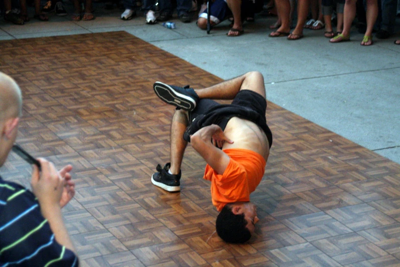 an orange shirted man is on the ground performing a trick