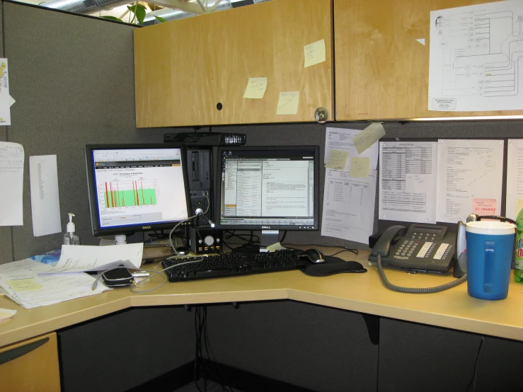 an office cubicle with two computer monitors and a telephone