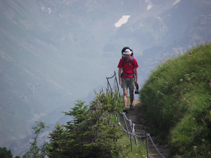 there is a male with a black and red backpack that is standing on a steep hill