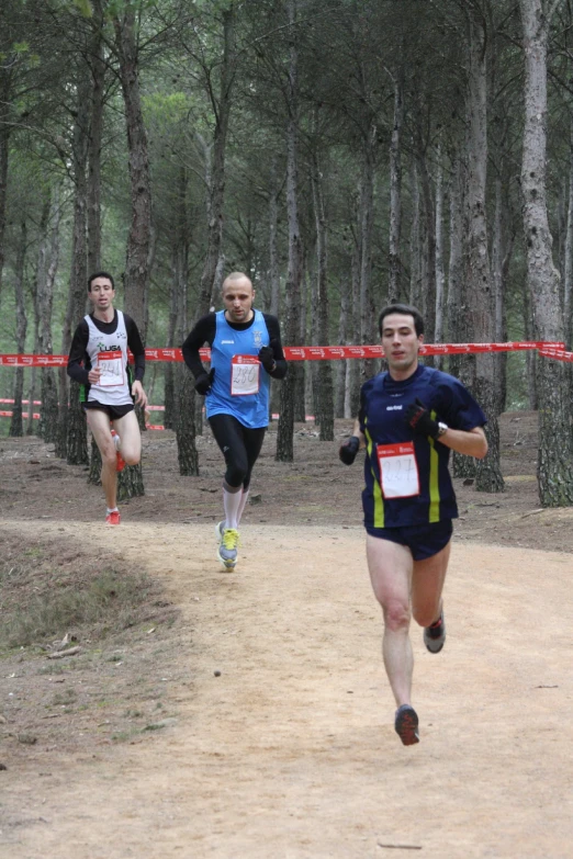 three men running on dirt path by trees