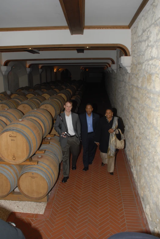 two men standing in between wooden barrels near some other people