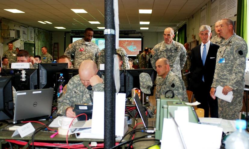 men in uniform stand around computers as others look on