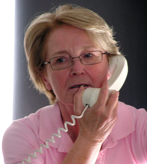 a woman with glasses uses an old fashioned telephone