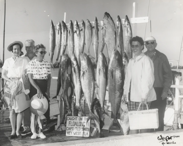 some people standing around large fish on the ocean