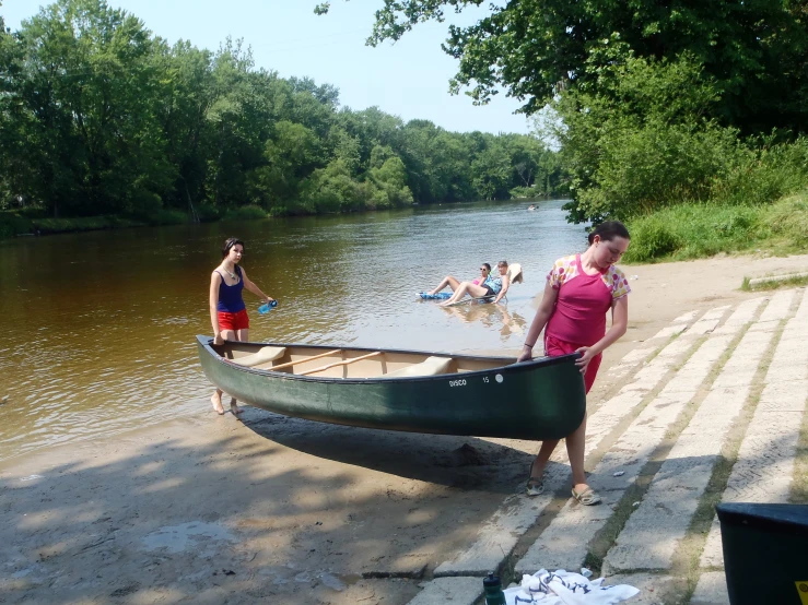 two women and children standing by the river by a green boat