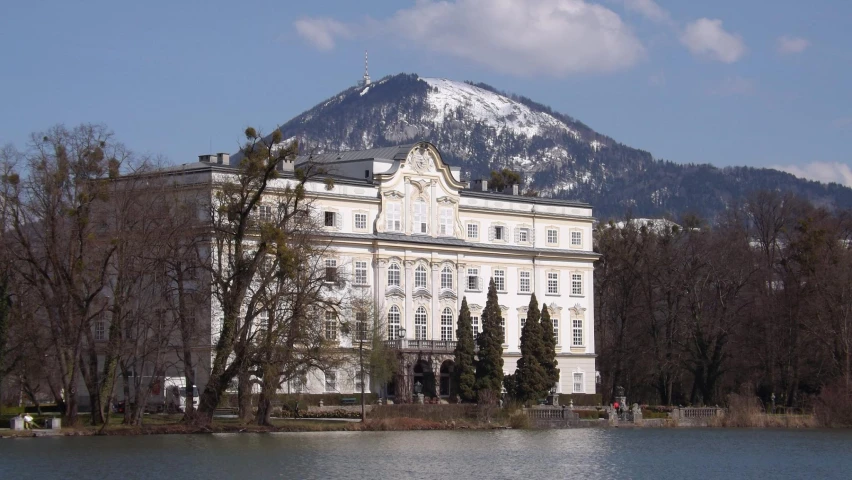 a building is near the edge of a body of water with a mountain in the background