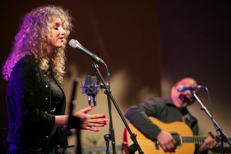 a woman holding a guitar and a man with a microphone behind her