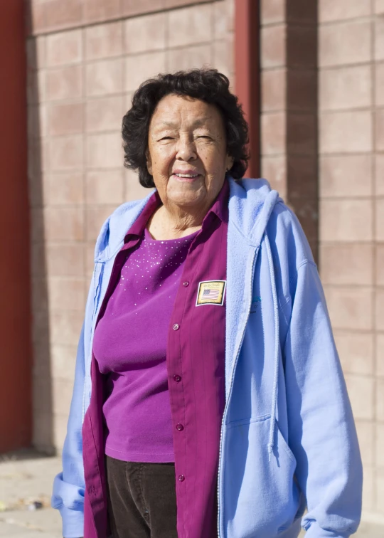 an old woman wearing a purple shirt standing next to a building