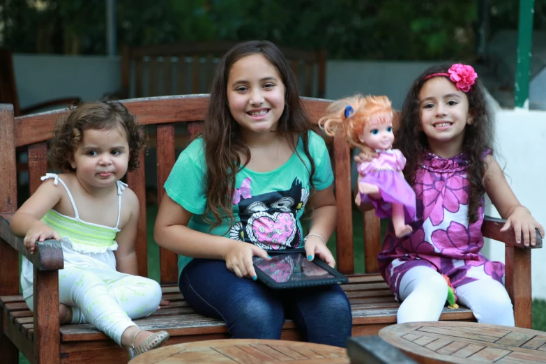 three little girls are sitting on a bench with dolls