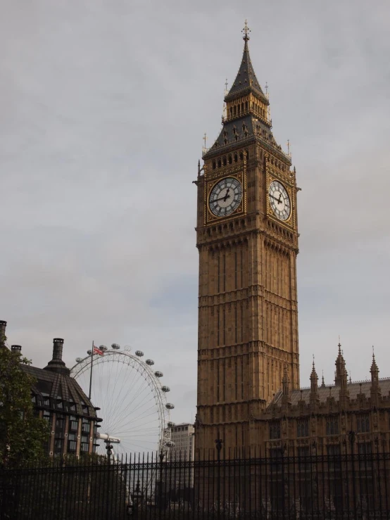 a very large clock tower with a ferris wheel in the background