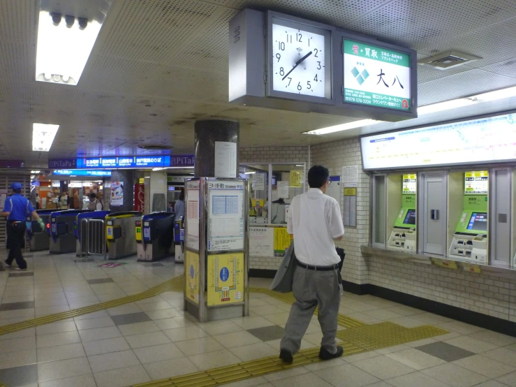 the man walks through an airport terminal with an electronic clock