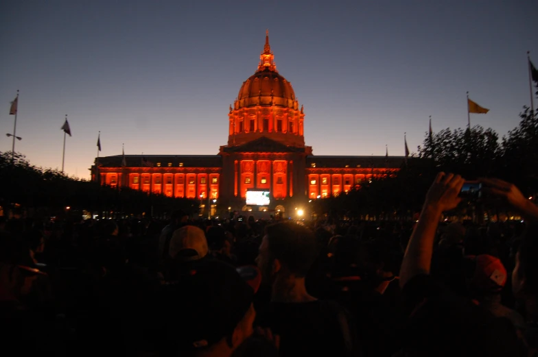 a crowd of people stand in front of the government building at sunset