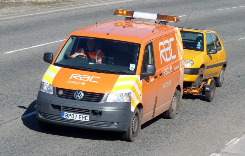 an orange van is towing another van down the road