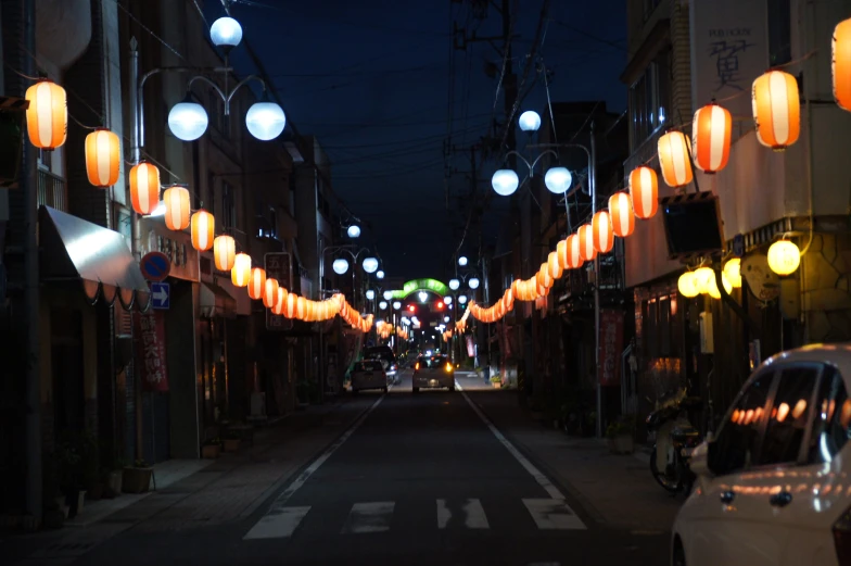 some bright lanterns line a street and cars are parked