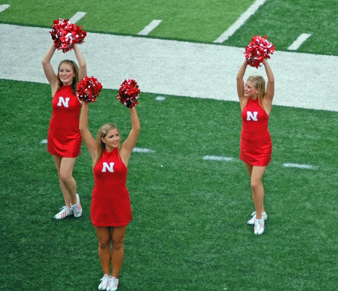 three cheerleaders wearing red on a football field
