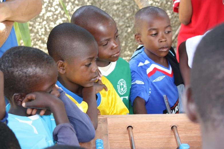 several children stand at a wooden table and look over the wooden plank