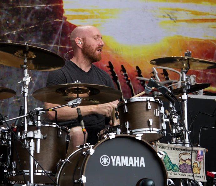 a bald man playing drums while wearing ear buds