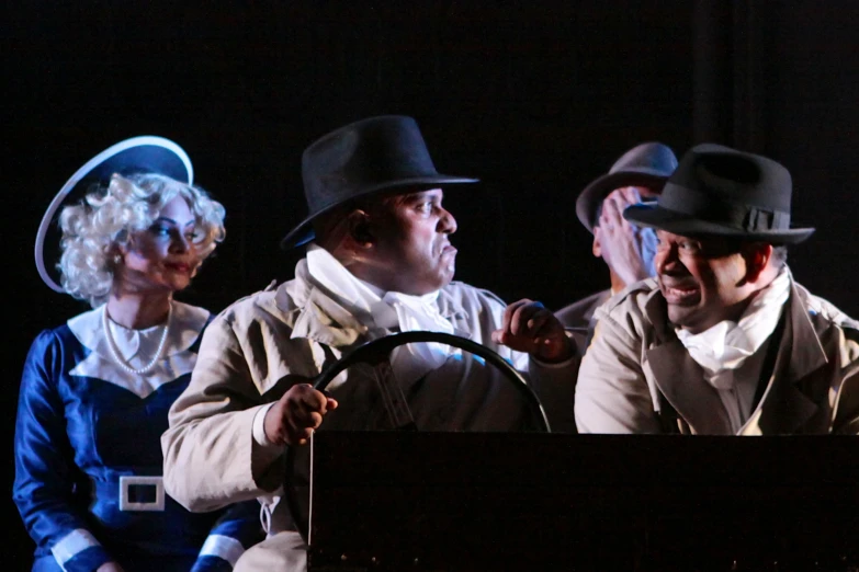 men in hats are on stage with two woman holding the steering wheel