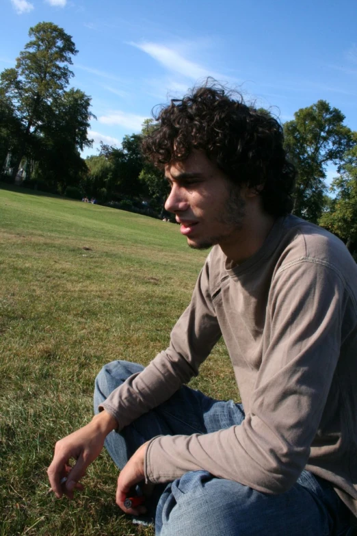 young man sitting on grass in front of grassy field with trees