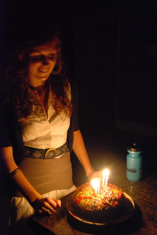 a woman is in the dark holding a small birthday cake with candles