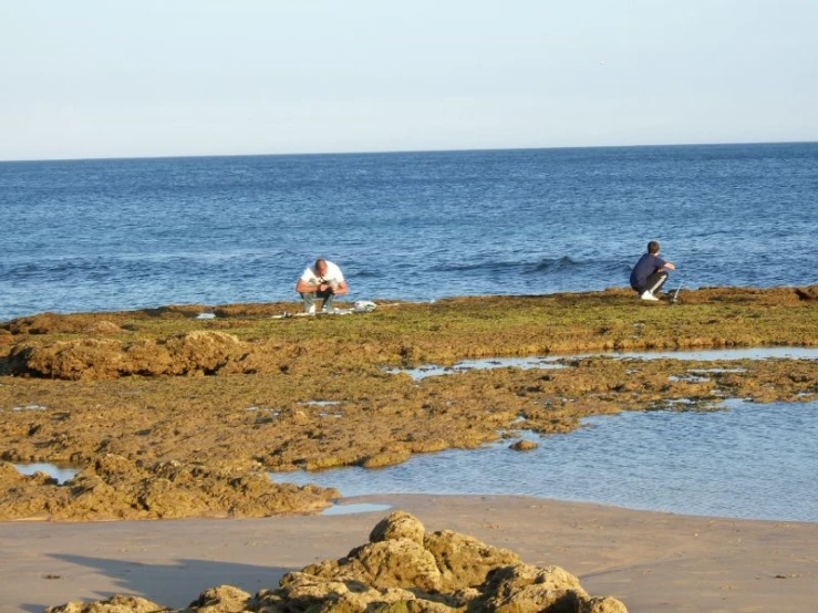 two people kneeling on rocks overlooking the ocean