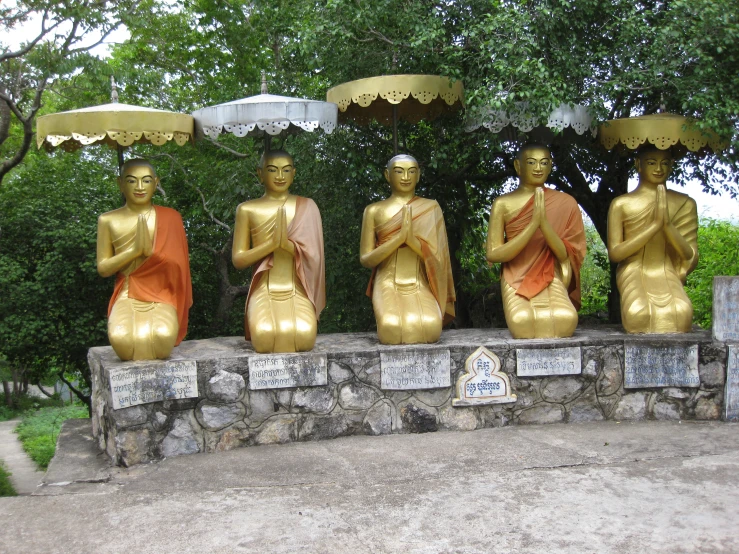 six golden buddha statues sitting on a stone slab