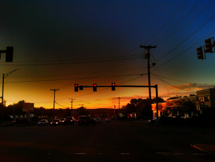 some cars are stopped at an intersection at sunset