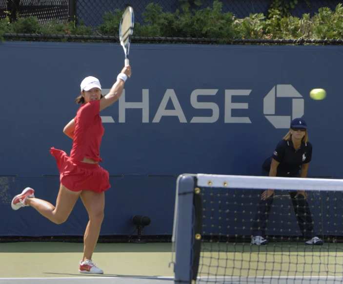 a woman wearing a red dress and white hat is playing tennis