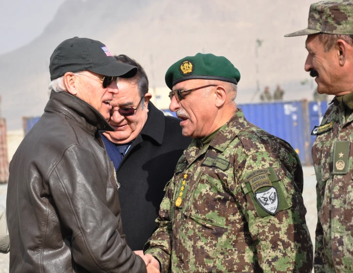 two men shaking hands with a man in a green hat