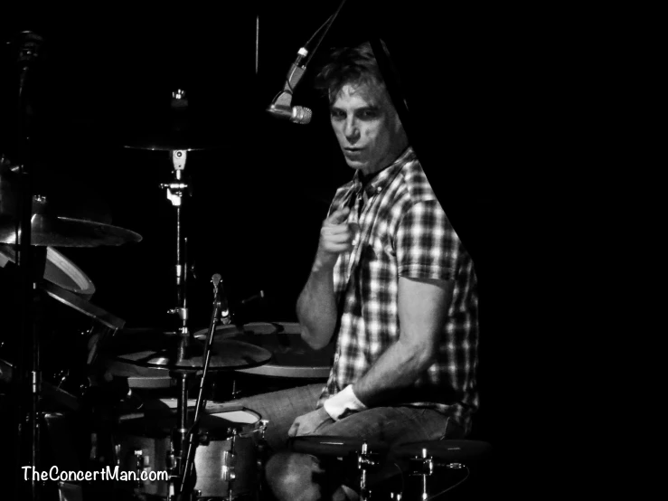 a man in plaid shirt playing drums and microphone