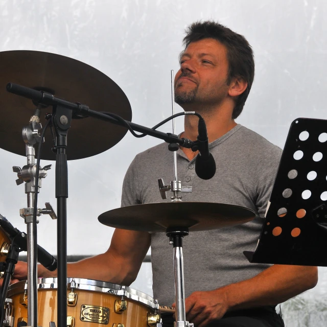 a drummer holding a black piece of equipment next to a drum set