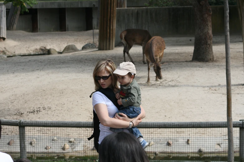 the baby is in his moms lap while they look at the giraffe