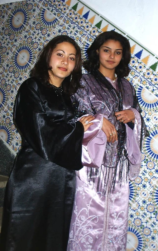 two woman standing together by a wall with designs