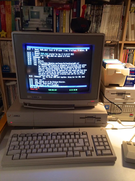 a computer with an old fashioned keyboard sits on a desk in front of a bookshelf