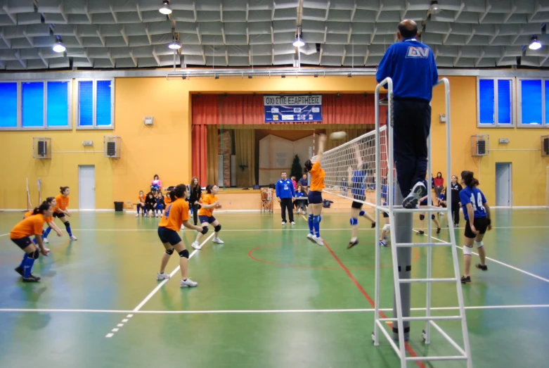 children in orange and blue uniforms are playing a game of volleyball