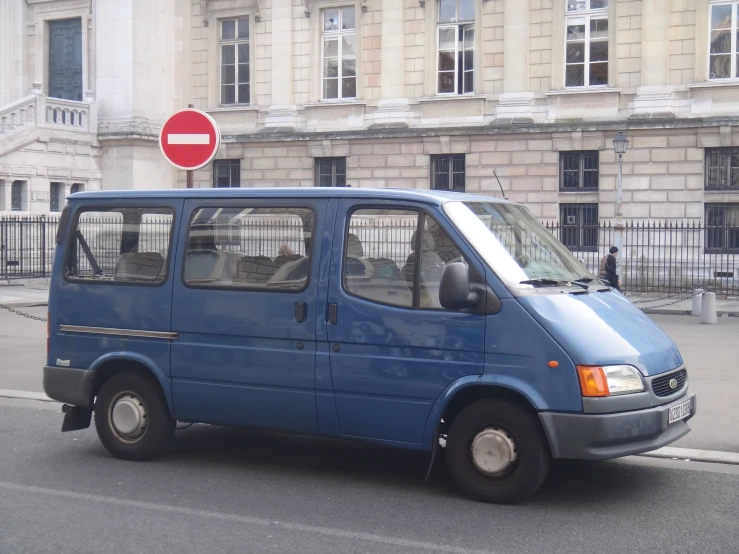 an empty blue van is stopped on a street with some traffic signs