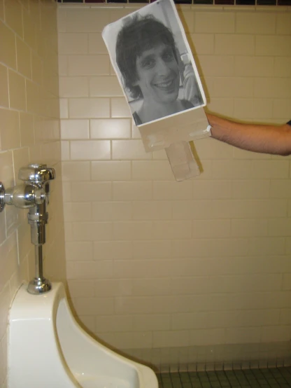 a man holds a po of his friend while he squates next to the urinal