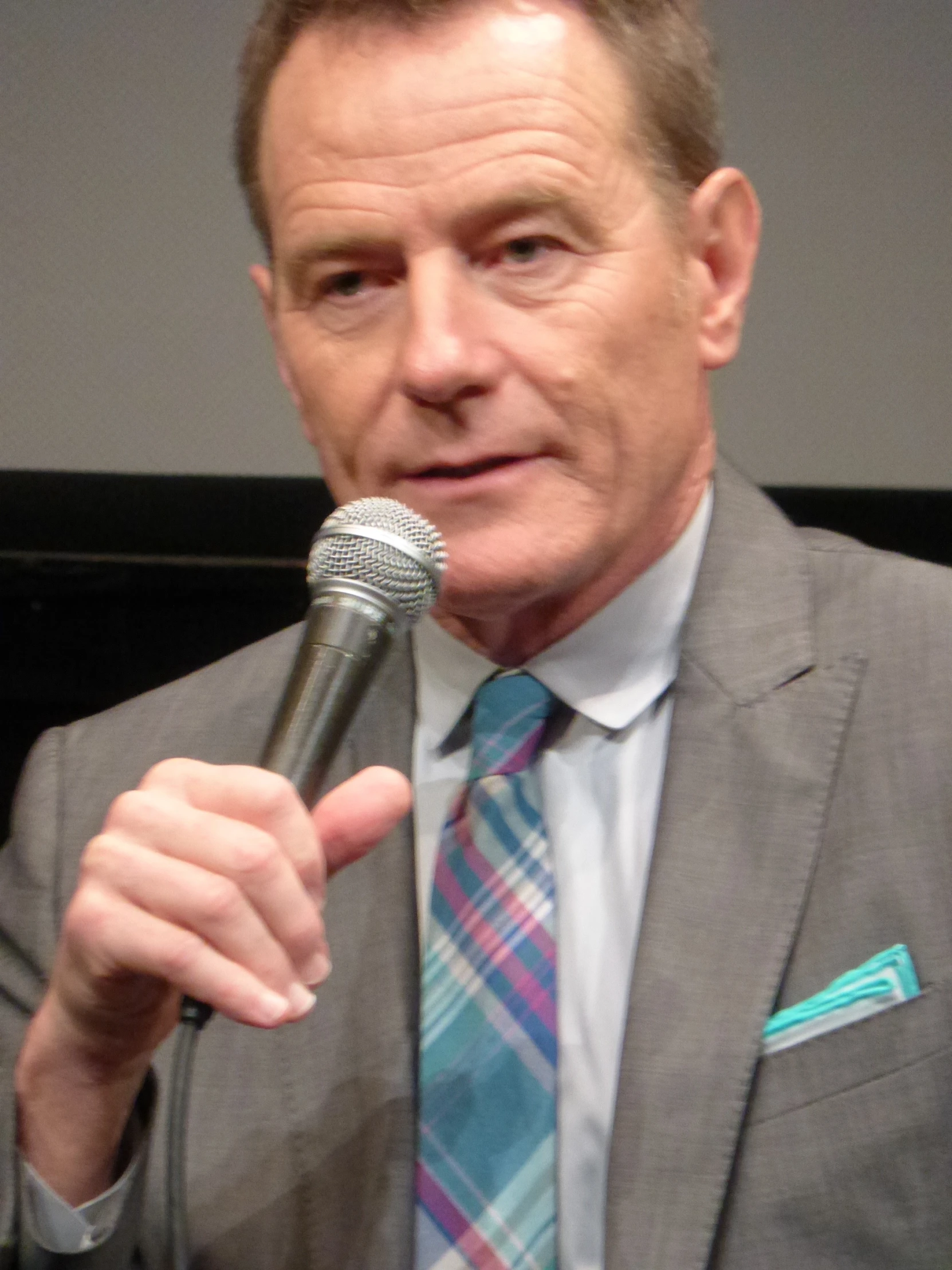 an older man in a grey suit talking into a microphone