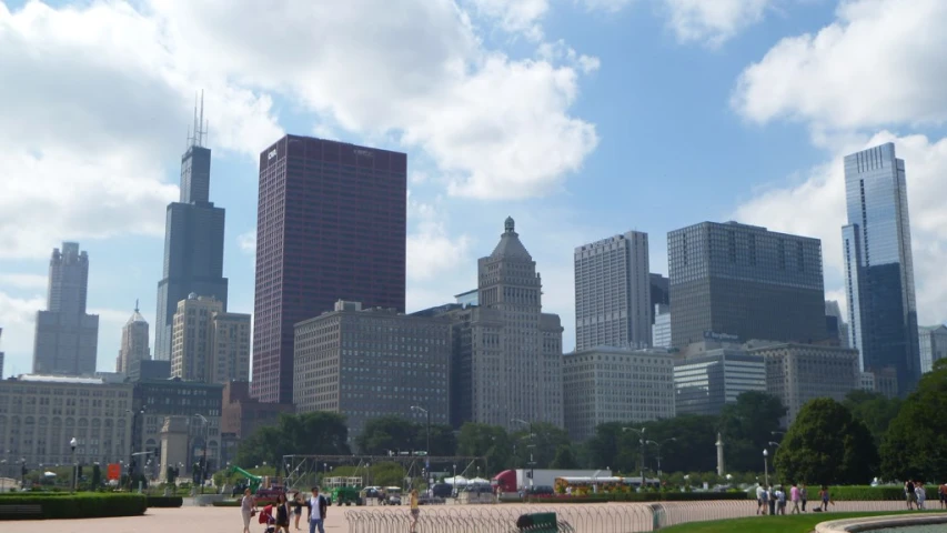 a park with a fountain in the foreground and people walking along