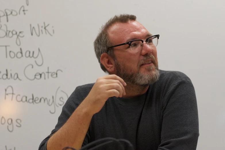 man with glasses in front of a white board