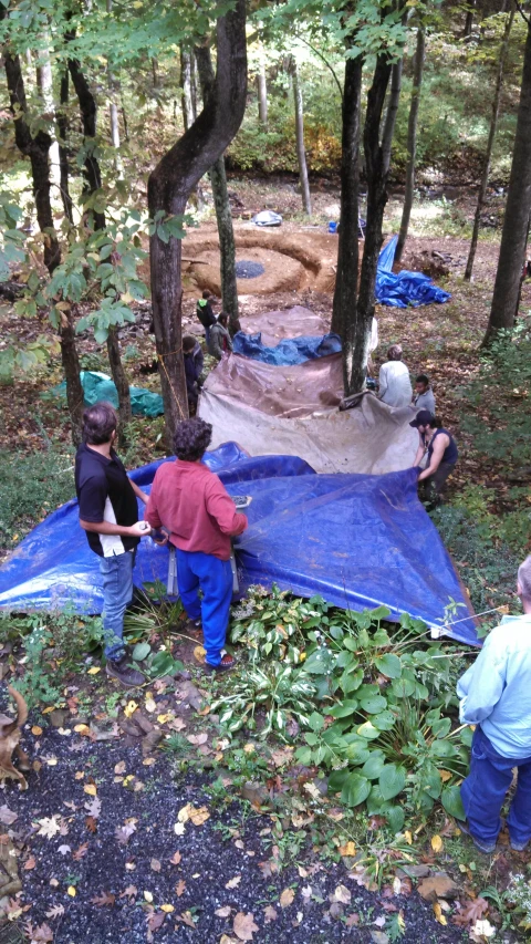 some people stand around in the forest near a tarp