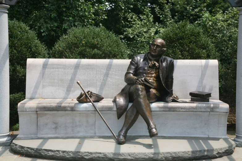 a statue of a man holding a cane sits on a white bench