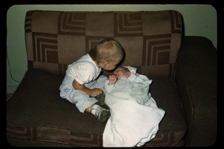 small boy sits on couch holding and nursing a newborn baby