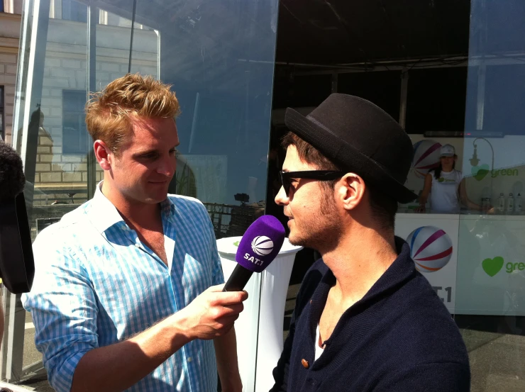 two men are talking to an announcer who is wearing a black hat